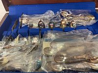 Photo showing multiple silver plated spoons in plastic wrapping inside compartments of a wooden box