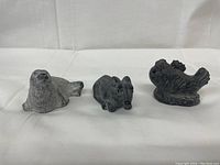 Soapstone sculptures of a seal, bear, and fish displayed side by side on white cloth background.