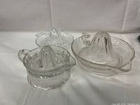 Three clear glass hand juicers grouped together showing different designs and sizes.