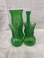 Four vintage green glass items displayed on a white background including vases and bottle with textured patterns