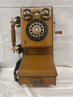 Front view of vintage wooden wall telephone with rotary dial, brass bells, wooden handset, and small drawer.