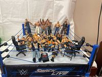 Wide view showing the WWE Smackdown Live Main Event ring with multiple WWE wrestler action figures placed inside and around it, some standing, some laying down, and some interacting with accessories like chairs.