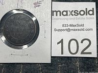 First Canadian penny dated 1876 secured in a square protective holder with MaxSold lot tag 102 near it.
