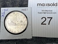 Front side of 1965 Canadian silver dollar showing the Voyageur design with two figures in a canoe, year and inscriptions visible.