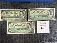 Top view of three Canadian Centennial $1 bills showing front design with Queen Elizabeth II portrait, serial numbers and signatures clearly visible.