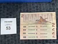 Four Canadian $2 bills with the back side showing two robins and serial numbers visible
