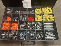 Overview of metal box with multiple compartments filled with yellow and orange plastic cable connectors, and multiple metal fittings including elbows and couplings.