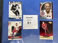 Four Gordie Howe hockey cards on blue background with lot number paper, showing different teams and styles