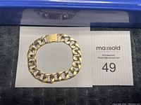 Gold curb link bracelet laid flat on MaxSold lot card