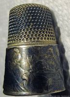 Close-up of silver antique thimble showing textured top and embossed child figure design on band.