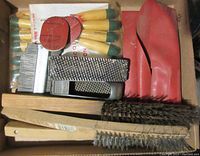 Box containing multiple carving tools with wooden handles and green tips, wire brushes, and metal rasps.
