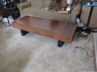 Front view of the rectangular mid-century modern wood coffee table with detached black legs placed on carpeted floor in front of a sofa.