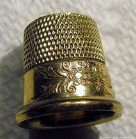 Close-up photo of the thimble showing the honeycomb textured top and floral engraved design on the side.