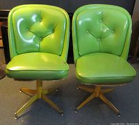 Two green vinyl upholstered swivel chairs with yellow painted metal bases shown from front view