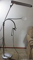 Full view of the OttLite 5-foot floor lamp with clamp arm and attached magnifier lens near beige couch.