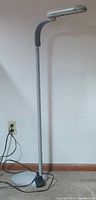 Full view of the white floor lamp approximately four feet tall with bendable neck and round base, plugged into electrical outlet.