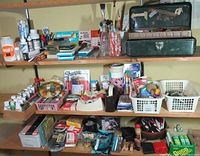 Wide view of wall shelves showing multiple paint bottles, brushes, color pencils, markers, glue, tape, stamps, and more organized in baskets and containers