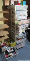 Wide view of the tall stacking plastic drawer cabinet filled with craft materials and supplies. Two open drawers partially visible with contents inside including craft materials.