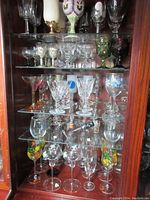 Full view of five shelves inside a wood cabinet displaying various glassware including clear, colored, and painted types, some marked Waterford.