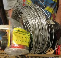 Large coil of thin grey wire with spool of orange wire and various insulated wires visible in a box
