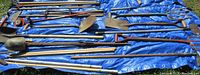 Overview of assorted yard tools laid out on a blue tarp outdoors, includes pitchforks, shovels, and cultivators.