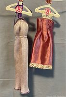Both Barbie evening dresses hanging side by side shown fully visible on white B-logo hangers.
