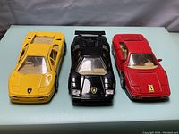 Front view of three die cast cars: yellow and black Lamborghinis, and red Ferrari