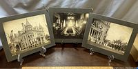 Three black and white mounted photographs displayed on a wooden table with display stands showing the exterior and interior of a stately home decorated with patriotic flags and a formal dinner scene.