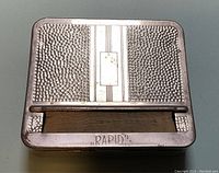 Top view of vintage RAPID cigarette rolling case showing hammered pattern and central striped panel with rectangular name plaque area