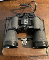 Photo of black textured binoculars with central focus knob labeled 'Insta Focus Bushell'. Shows body and lenses clearly.