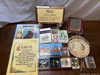 Overview of religious prayer cards, children’s books, wooden plaque, and rosary beads arranged on a table.
