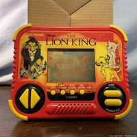 Front view of the red handheld electronic game with yellow buttons and screen showing The Lion King graphics