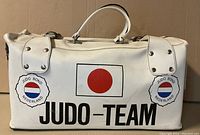 Front and side view of white leather Judo sports bag with Japanese flag and Judo Bond Nederland logos, showing handles and zipper closure.