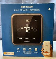 Front of the Blue box showing Honeywell Lyric T5 WiFi Thermostat with image of the thermostat and smartphone app compatibility icons.