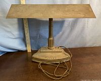 Front view of the vintage lamp showing the rectangular metal shade, central column, cast iron base with push buttons and attached braided cord, ruler for scale.