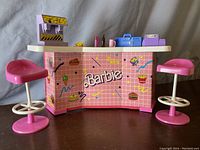 Full front view of Barbie snack shop counter with two pink stools, showing overall condition and decorative details including the Barbie logo and snack graphics.