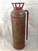 Full view of the copper foam fire extinguisher with red handle and brass information plaques visible.