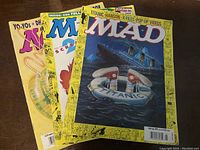 Three Mad Magazine issues spread on table showing front covers with colorful satirical artwork and titles from late 1990s.
