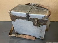 Closed military test set box with worn green and silver paint, leather shoulder strap attached.