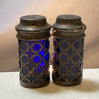 Front view of the pair of vintage cobalt blue glass and sterling silver cutout salt and pepper shakers showing tarnished silver tops and geometric pattern on the silver casing.