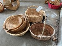 Nine assorted woven baskets displayed on concrete floor, varying sizes and handle types visible.