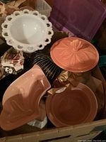 Set of pink ceramic bowls and dishes including one with a floral embossed lid and an angular dish, alongside white decorative bowl and black metal rack.