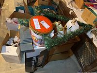 Box with Christmas ornaments, pinecones, and large metal or plastic flat gray panels, surrounded by green garland.