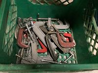 Top-down view showing various sizes of metal C-clamps inside a green milk crate.