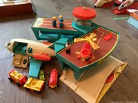 Top view of vintage Fisher Price airport playset with terminal, airplane, helicopter, vehicles and play figures arranged on wooden floor.