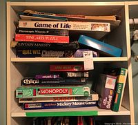 Two shelves stacked with various vintage board games and puzzles with visible titles including Monopoly, Game of Life, Chaos, and Mickey Mouse Game.