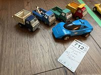 Five vintage toy vehicles displayed on wood floor; blue Kenner Lancia race car and four Marx metal trucks in various colors. Wear and paint loss visible.