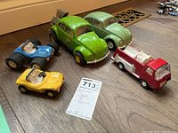 Five metal toy vehicles arranged on a wooden floor including two Volkswagen Beetle dune buggies, classic Beetle, red firetruck and two dune buggies.