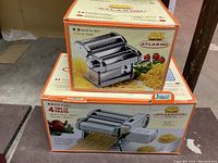 Boxes showing the Marcato Atlas 150 pasta maker and the Marcato Atlas motor with pasta cutters and product branding.
