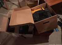 Three boxes on floor with photographic accessories inside, various items and boxes visible